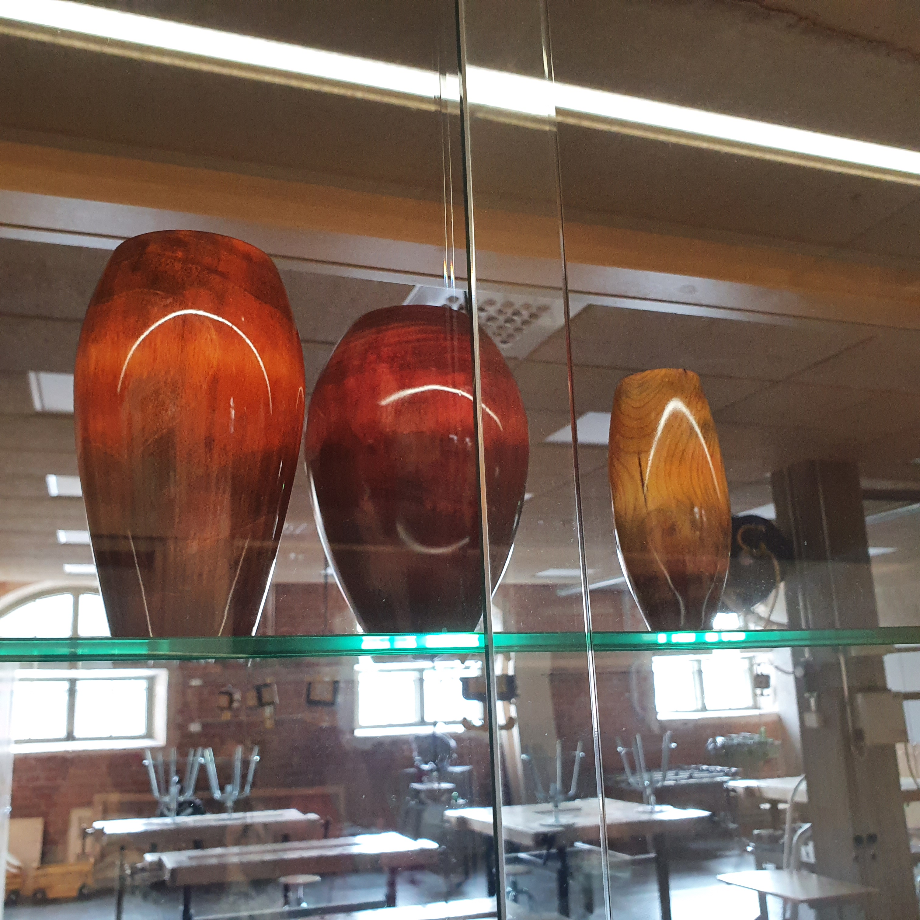 Three wooden vases in shads of red and orange in a glass display case