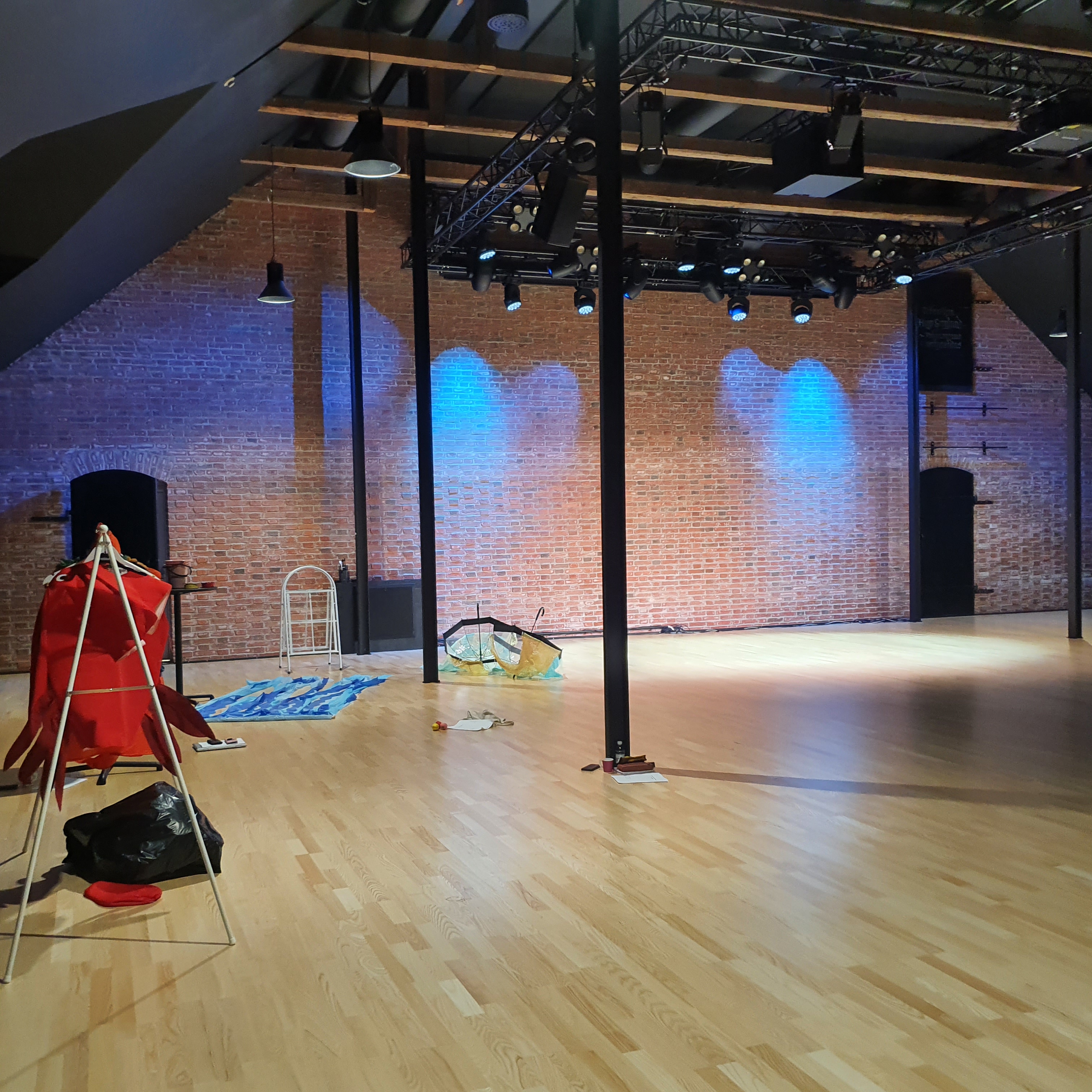 A wide view of Hugo Sali showing a red brick wall at teh far end with black pillars and a light coloured wooden floor