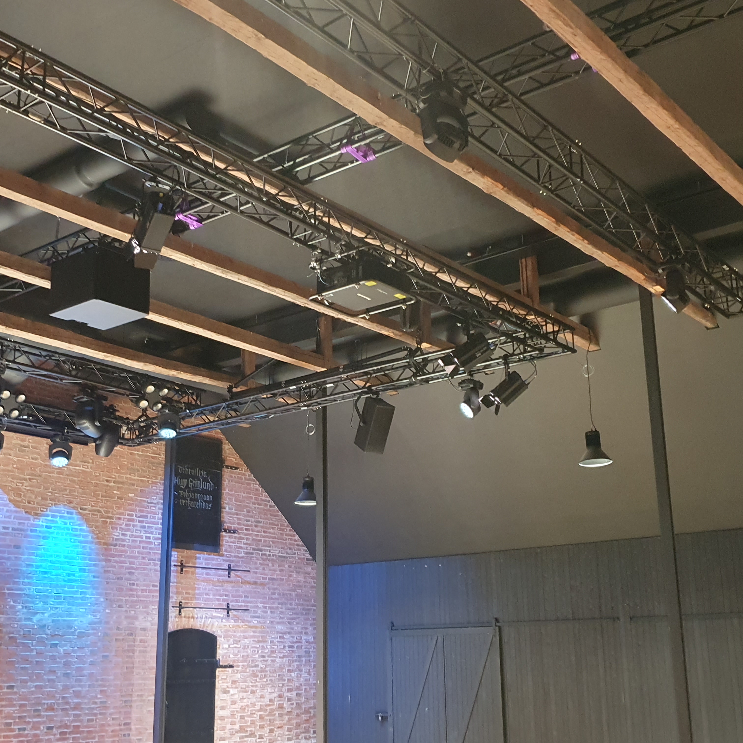 Light wood coloured beams against a black ceiling. In the background is a red brick wall and a black wooden wall