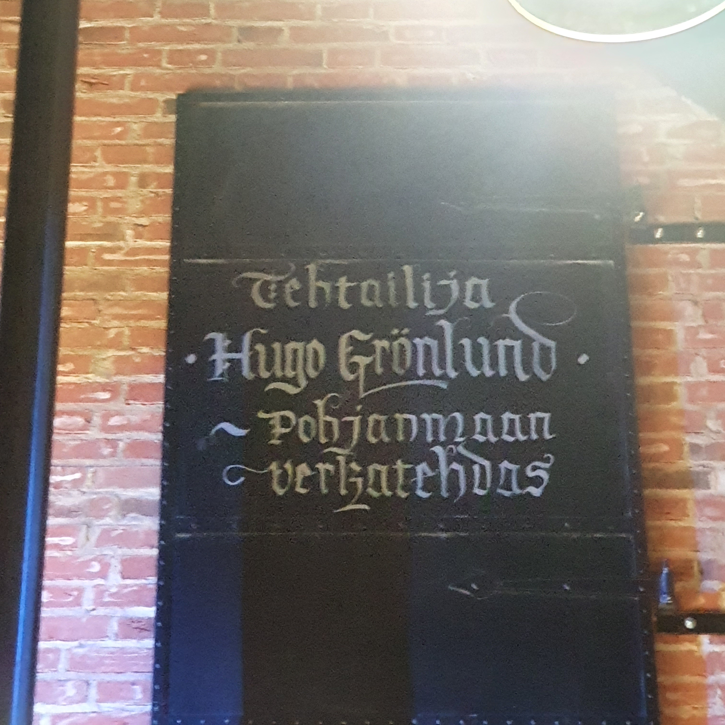 Black door in a red brick wall with the name Hugo Grönlund in white script