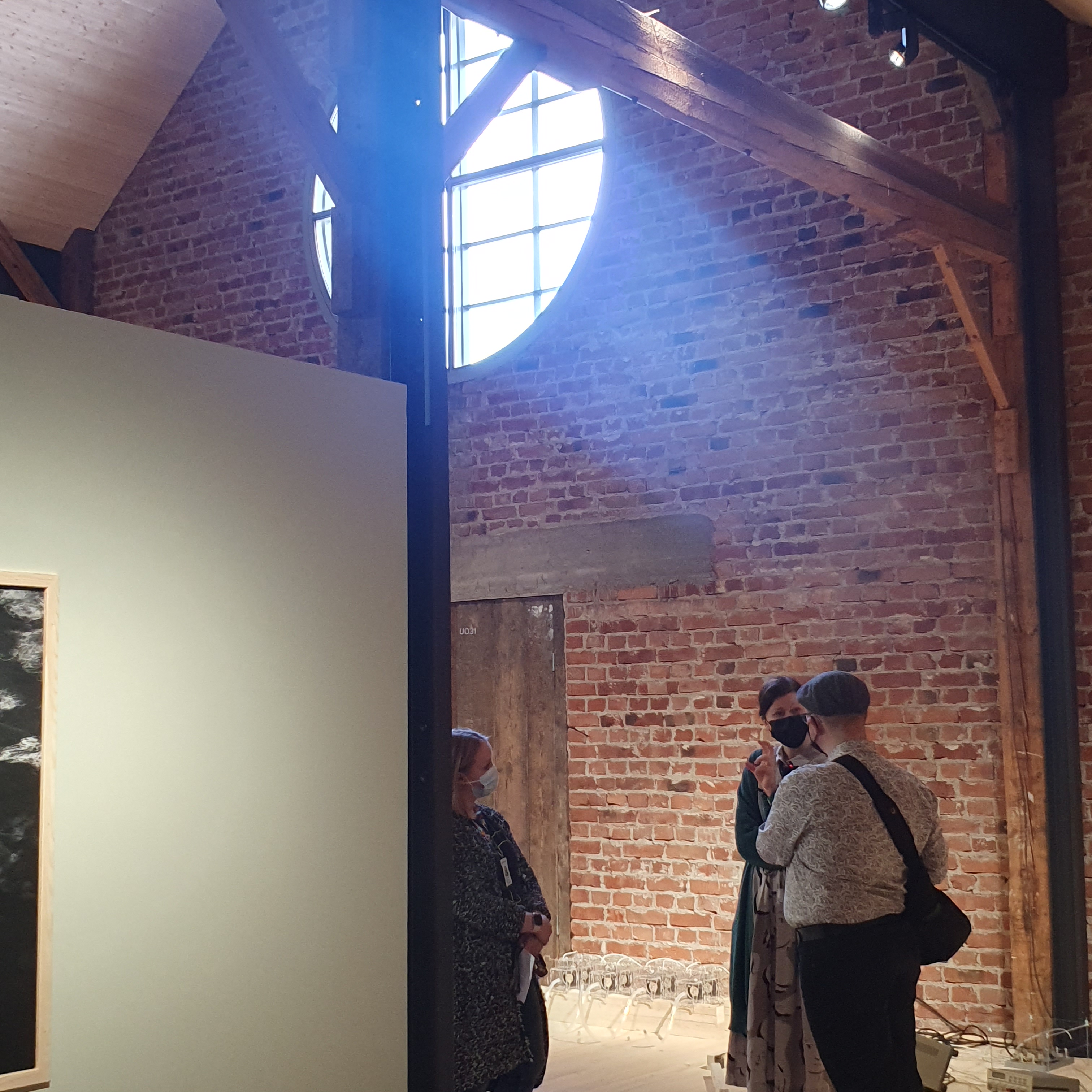 Mark, Paäivi and Elina standing below a round window in front of a red brick wall