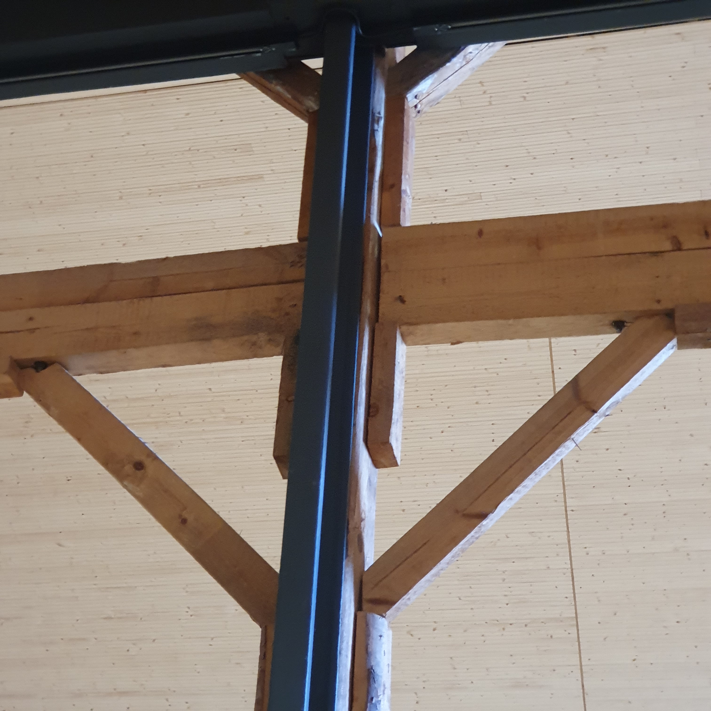 Black metal pillars reinforcing dark wood pillars and beams against a background of a light wooden ceiling.