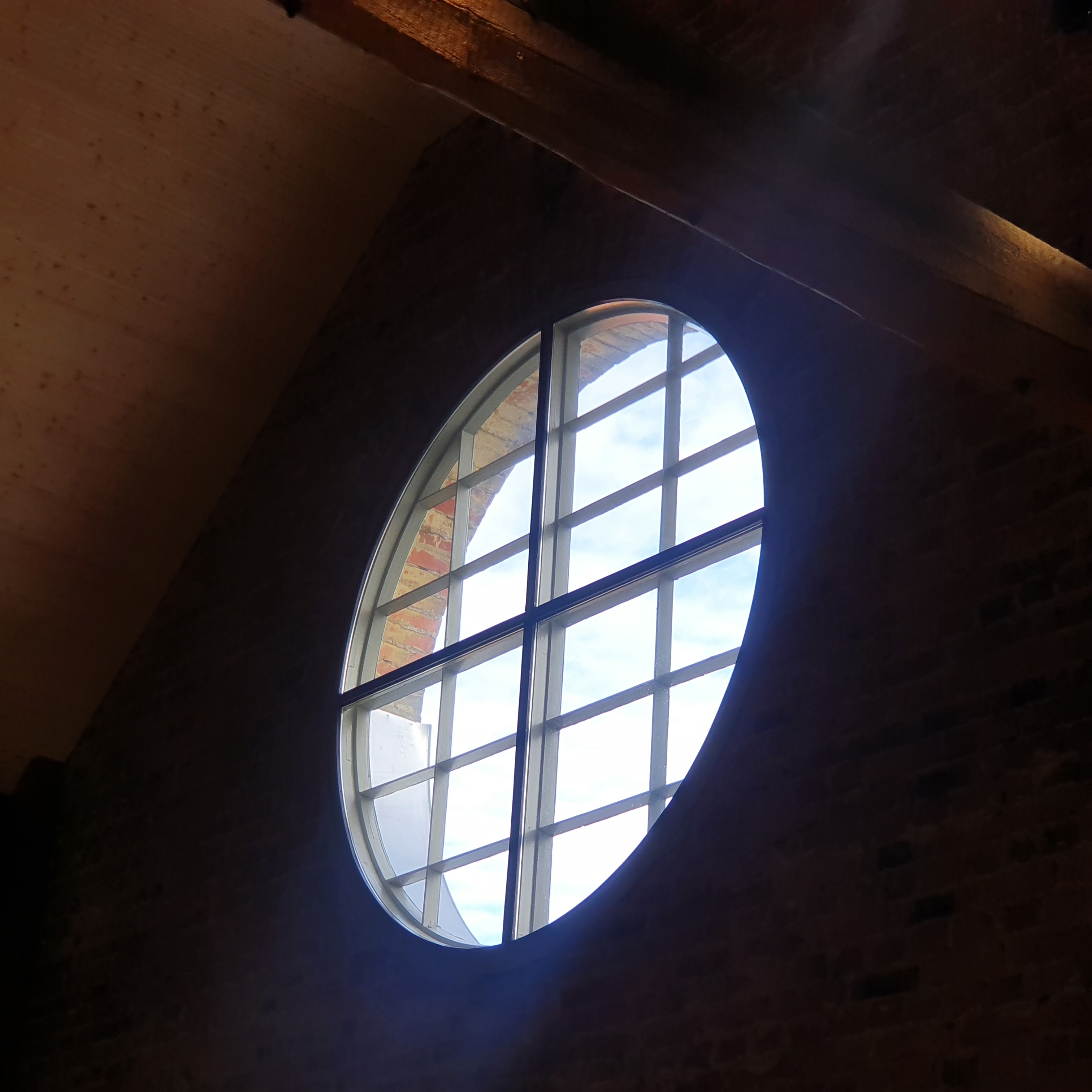 Round window lit from outside. Red brick wall is dark in contrast to the light.