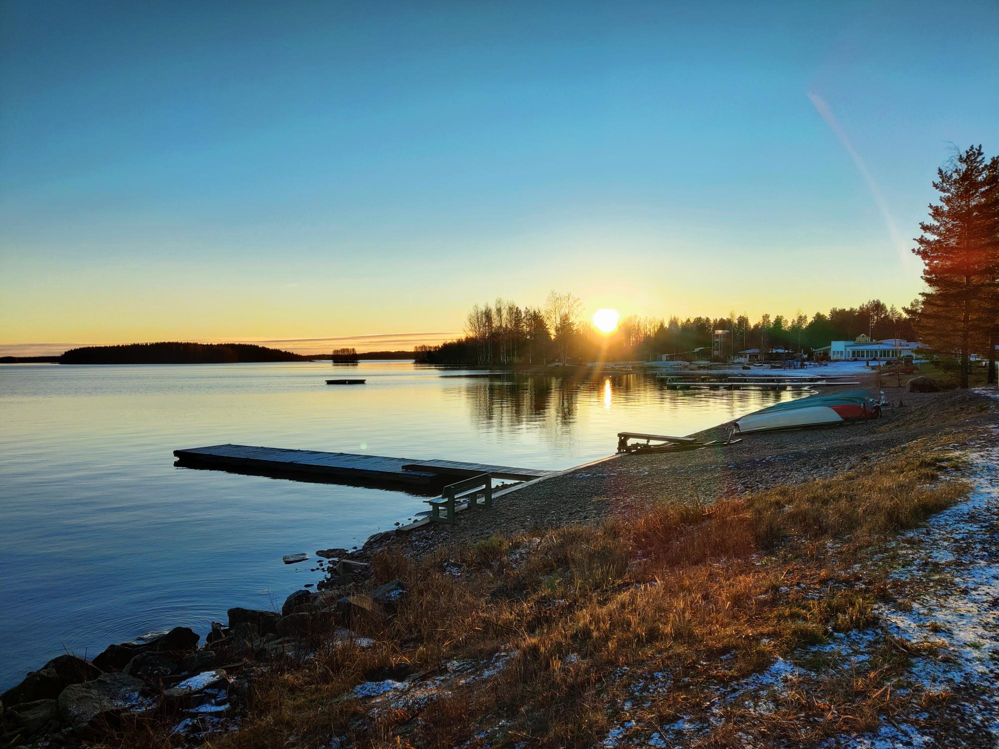 The sun setting over Lake Kalajärvi in late-winter. The lake is unfrozen but there is snow on the shoreline
