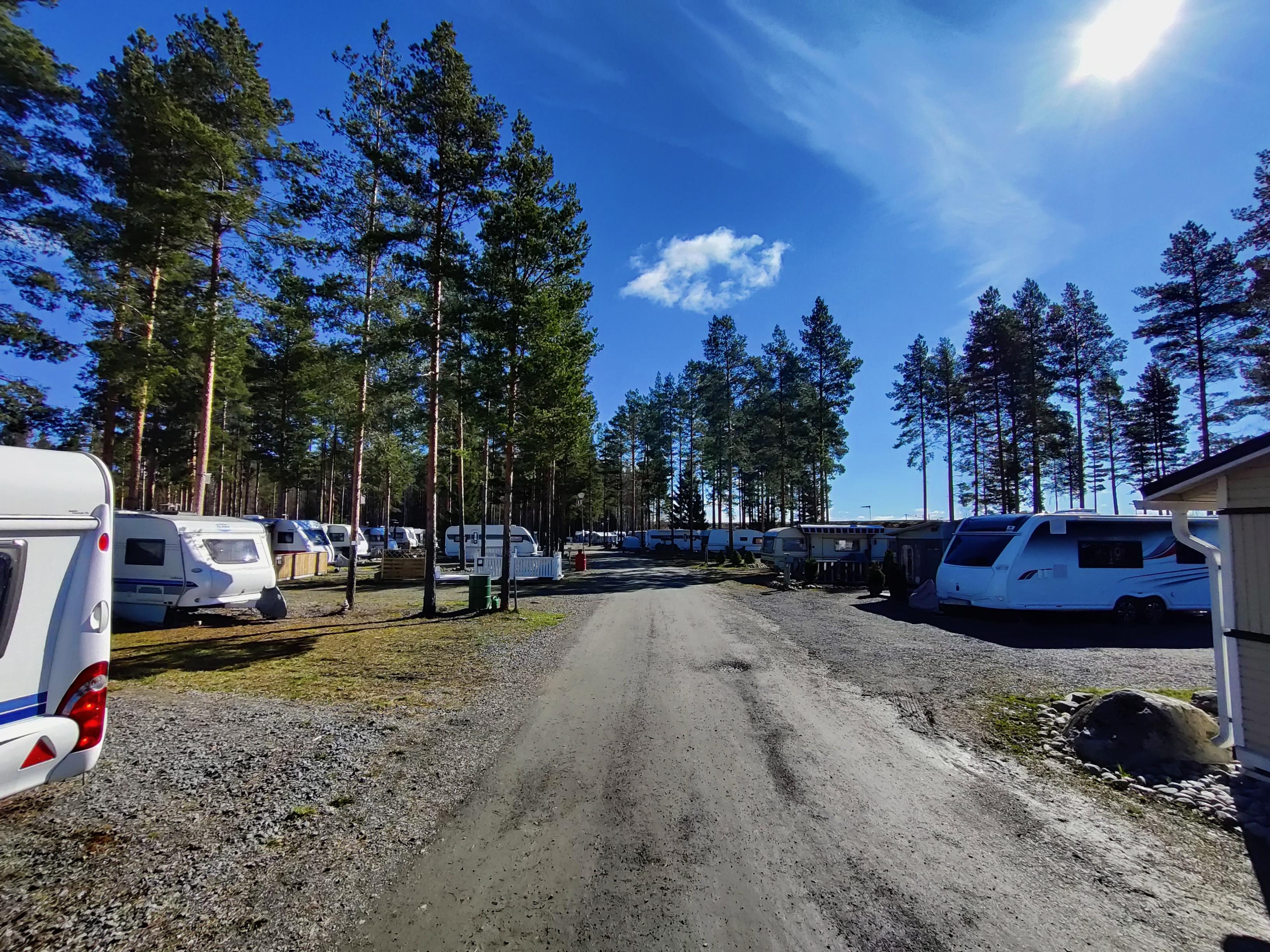 Caravans either side of the road through SF-Caravan-Kalajärvi with tall trees and a blue sky