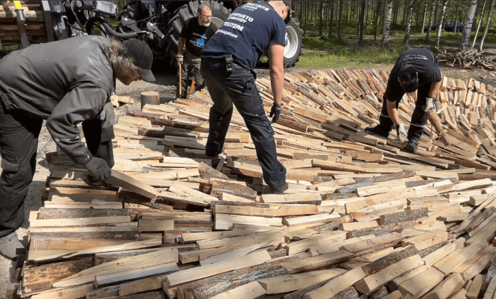 Three men placing small wooden logs to build a tar pit.