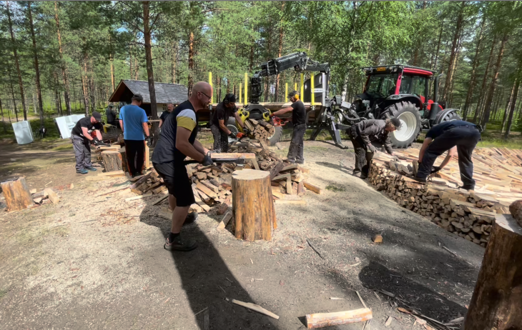 A group of men with various tools, chopping wood. Man in foreground chopping wood with an axe.