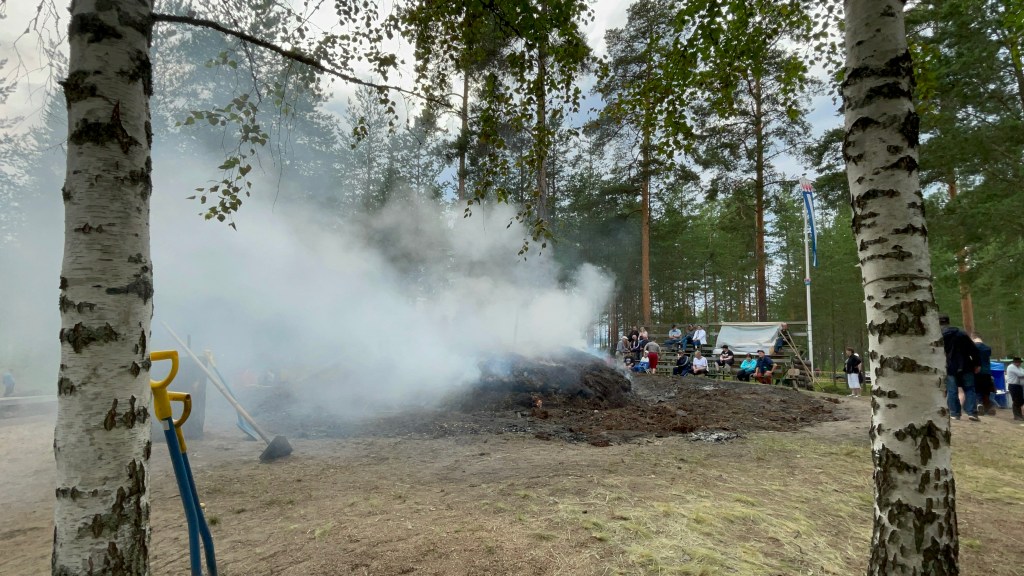 Smouldering fire pit with billowing white smoke, framed by two silver birch trees..
