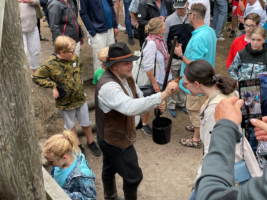 A man in traditional costume blesses a brunette woman with a spot of tar on his forehead.